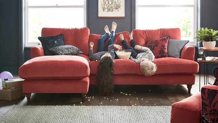 Two children laid upside down with food all over on a red velvet sofa