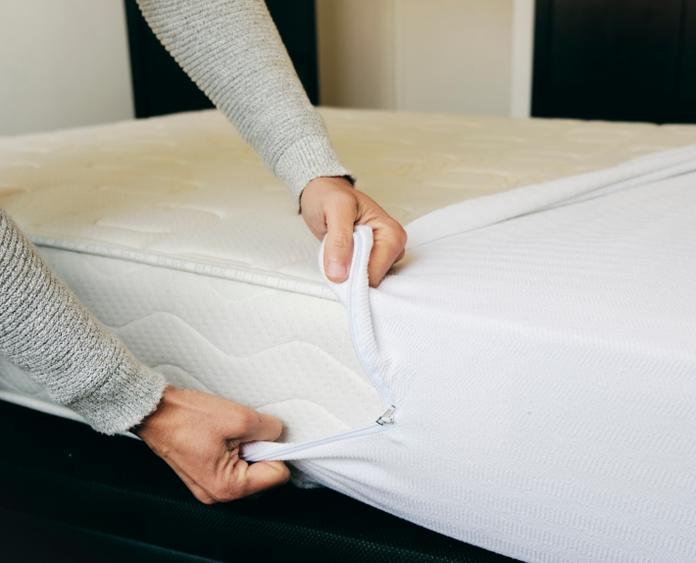 person in a grey jumper pulling on a white mattress protector