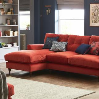 Red corner sofa with blue decorative scatter cushions in a cosy living room with dark blue walls