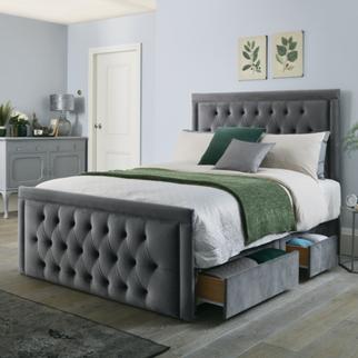 Dark grey quilted bed with storage drawers and white bedding with a green throw and cushions