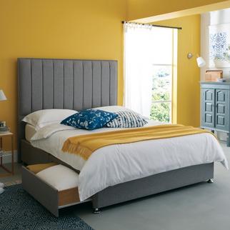 Grey divan bed with storage drawers against a yellow wall with white bedding and a yellow throw
