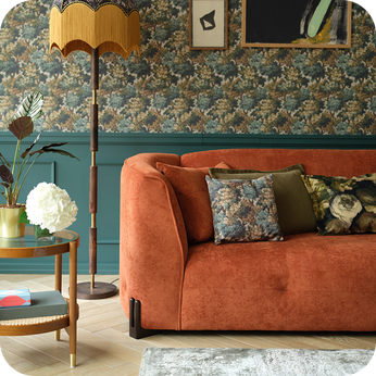 Rust curved sofa on top a wooden with against a teal wall with patterned wallpaper