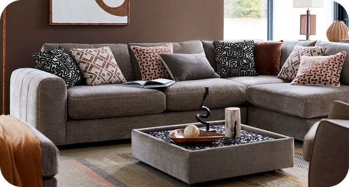 Dark brown corner sofa with brown patterned scatter cushions against a brown wall