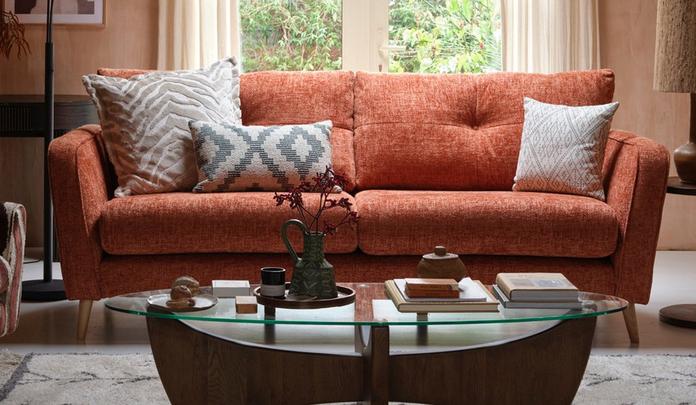 Brown mid century chenille sofa with pattern scatter cushions next to a walnut and glass coffee table
