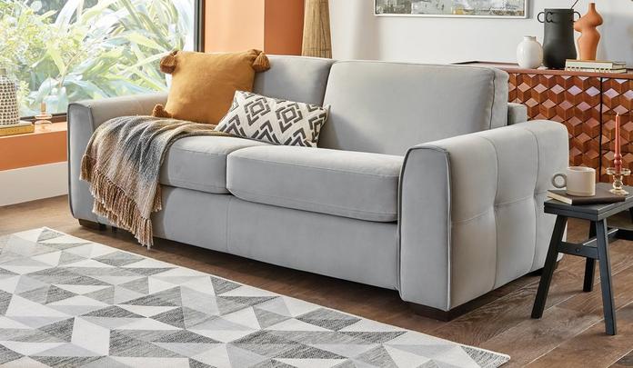 Grey quilted chenille sofa with a orange and pattern scatter on a dark wood floor and pattern rug