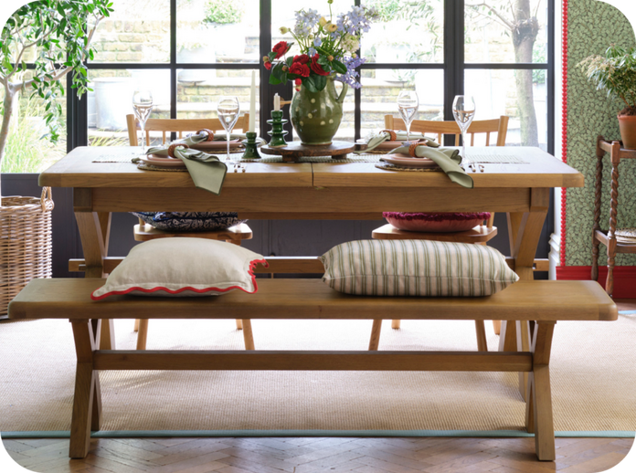 wooden dining table with two chairs and a bench with two scatter cushions sat on the bench next to a large window