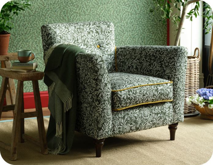 green floral accent chair with gold trim, a green throw thrown over the arm against a green leafy wall with pink skirting
