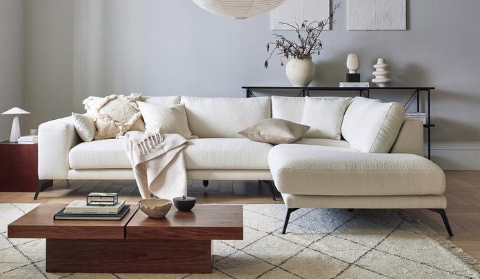 white boucle corner sofa with blankangled legs next to a dark wood coffee table on a fluffy rug