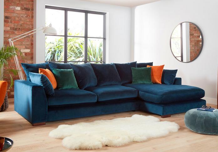 blue velvet corner sofa with green, orange and blue scatter cushions next to a white fluffy rug