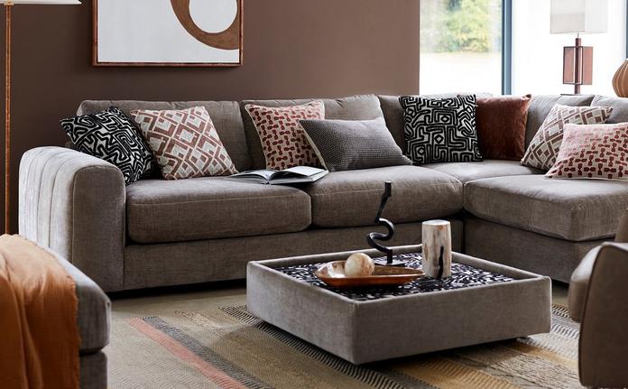 dark brown corner sofa next to a brown wall finished with a variety of brown and monochrome scatter cushions