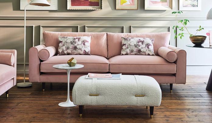 pink velvet sofa with round bolster cushions next to a boucle footstool and white side table