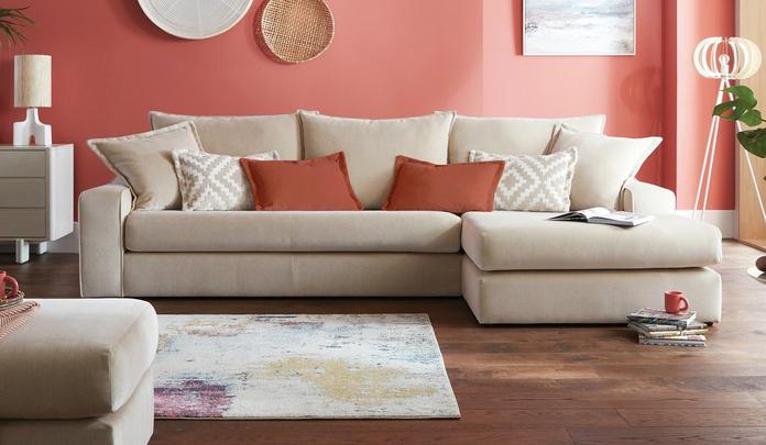 beige corner sofa with orange and pattern scatter cushions against a peach wall
