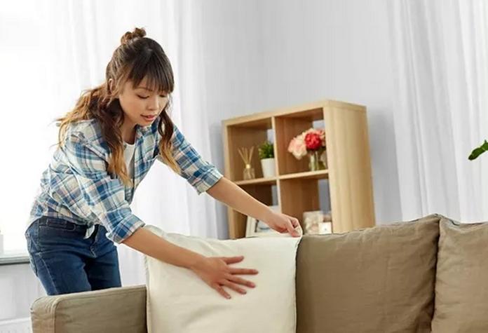 a young smiling omen smoothing and plump a scatter cushion on a beige sofa
