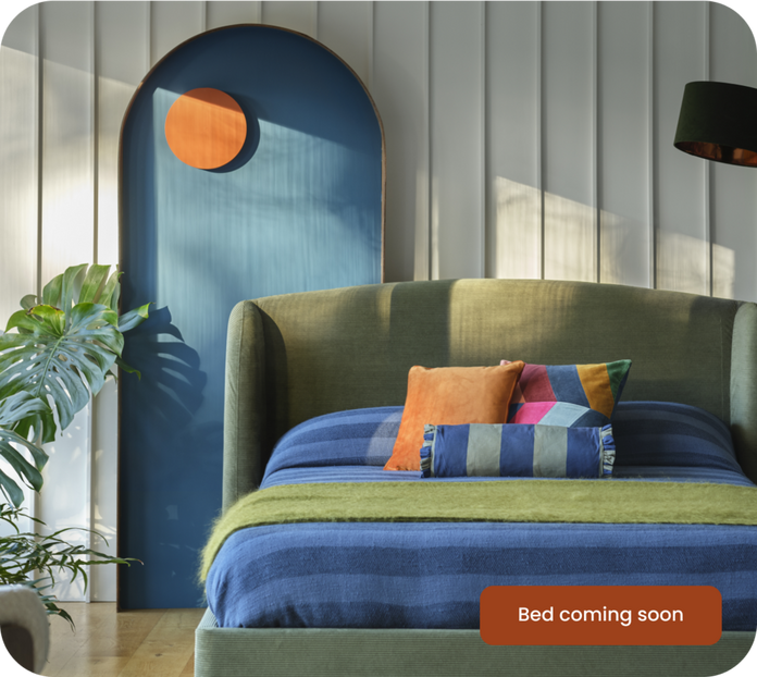 Green divan bed with blue and green bedding against a panelled wall and wooden flooring