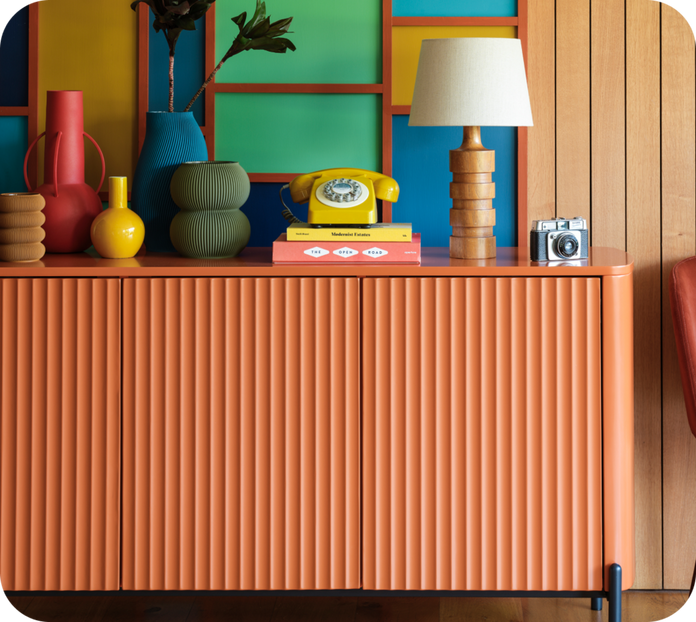Orange sideboard with black metal legs topped with various colourful accessories and artwork