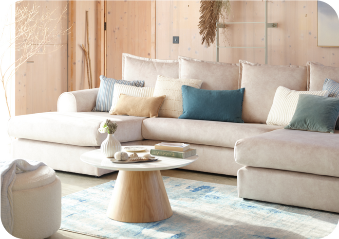 Neutral living space with a beige sofa finished with blue and teal cushions and rug against a light wood wall