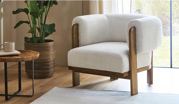 white boucle tub chair with wooden frame next to a large window on a dark wood floor