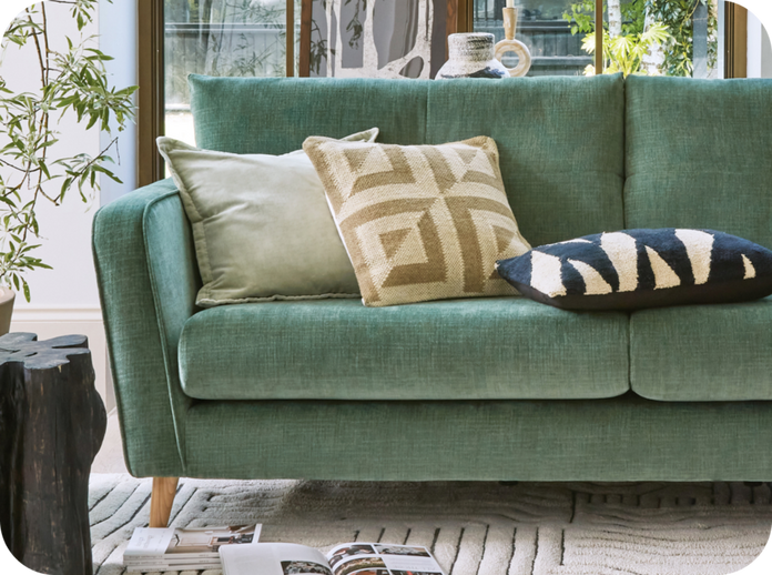green sofa with wood angled feet and different coloured patterned cushions against a large window