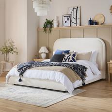 cream boucle bed against a beige panelled wall with a blue throw and scatter cushions 