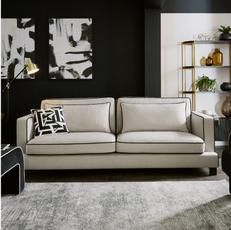 light grey sofa with black piping around the edge next to a black footstool with white piping