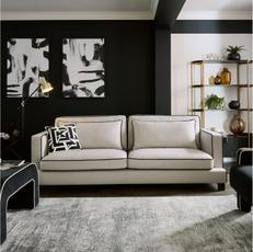 white sofa with black trim around the edge against a black wall and next to a white fluffy rug