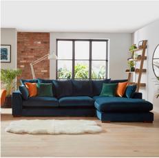 velvet blue corner sofa with orange, green and blue velvet scatter cushions next to a white fluffy rug