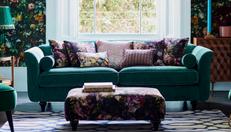 Teal sofa with floral scatter cushions and footstool with matching floral wallpaper
