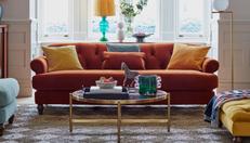 Orange Chesterfield sofa with yellow scatter cushions next to a gold coffee table