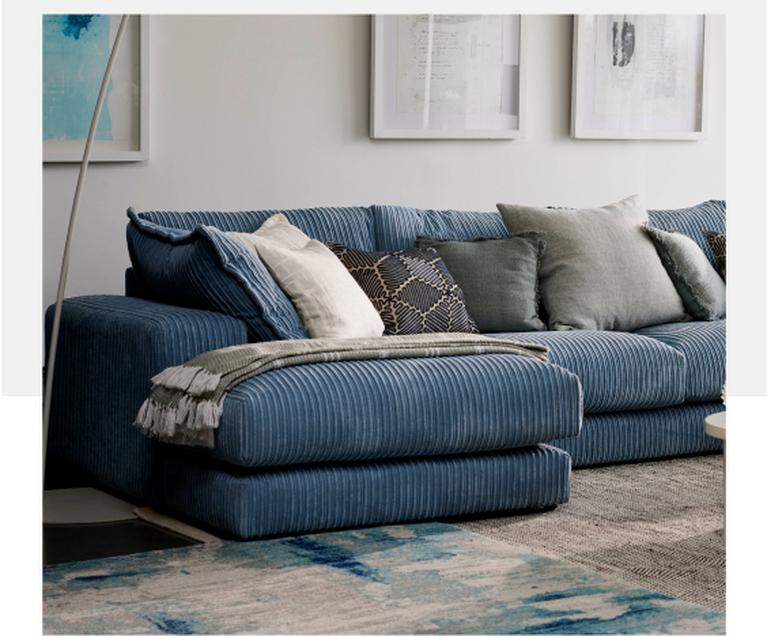 blue jumbo cord double chaise sofa with a mixture of different scatter cushions next to a white round nest coffee table