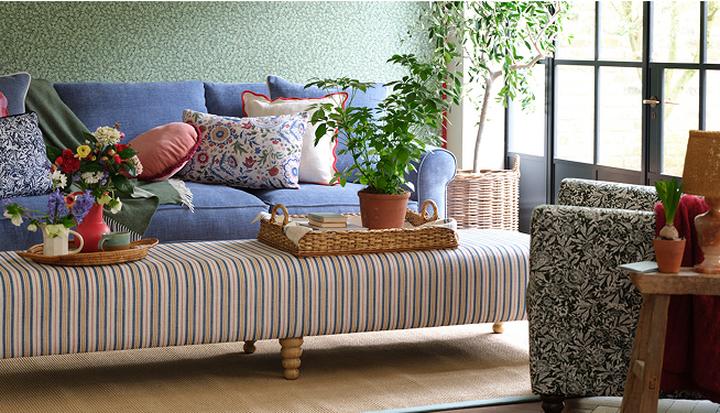 blue fabric sofa with a selection of floral scatter cushions next to a striped footstool with floral accent chair