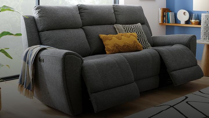 dark grey recliner sofa with orange scatter cushions next to a blue wall with oak shelves