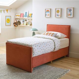 orange single bed with polka dot bedding and a grey fluffy rug with colourful pictures and books