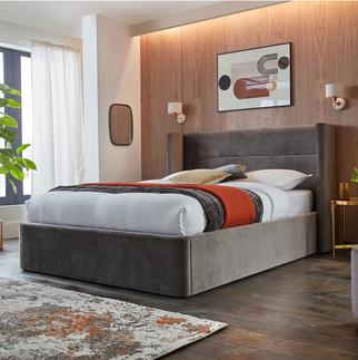 dakr grey velvet ottoman bed with a brown and orange throw against a wood wall next to a colourful rug