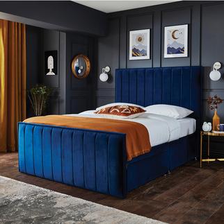 navy blue velvet bed against a dark grey panelled wall with an orange throw