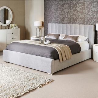 light grey ottoman bed next to a cream fluffy rug with a brown bedding set and cream throw