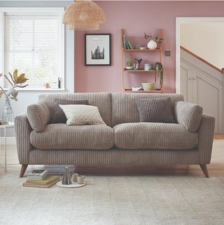 beige jumbo cord sofa with wooden angled feet against a pink wall