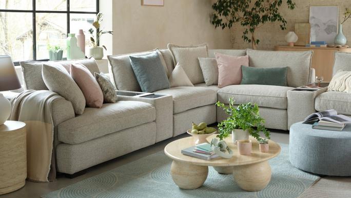 cream corner sofa with pastel pink teal and beige scatter cushions with a blue rug