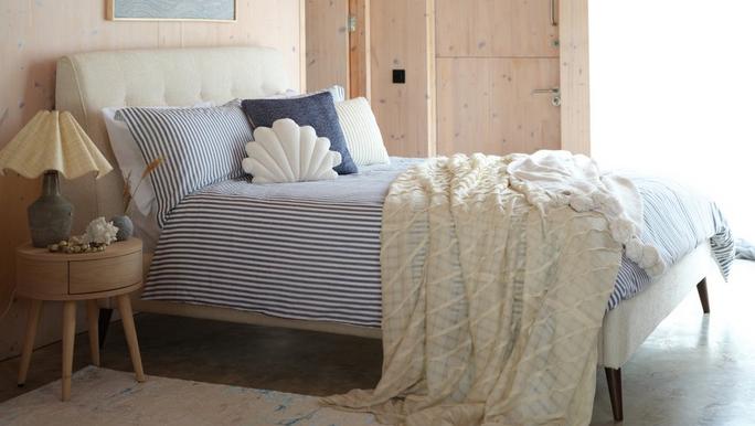 white boucle bed with blue stripe bedding toppped with a cream throw next to a wooden wall