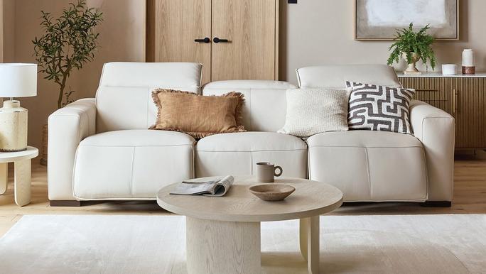 beige leather recliner sofa on a wooden floor next to a white fluffy rug with white coffee and side table