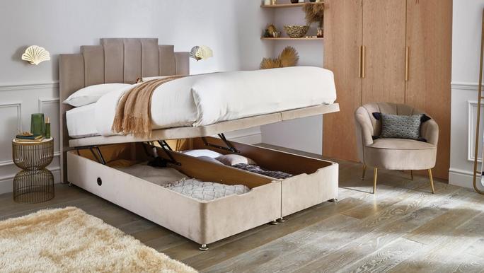 Niamh double ottoman bed frame in mink velvet fabric, shown open in a neutral room with matching accent chair.