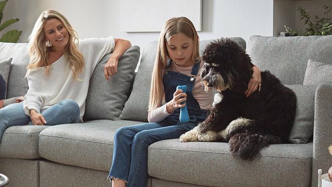 Smiling mum sat on sofa looking on to her young daughter and dog playing on the sofa