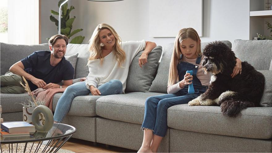 young family smiling with child and dog on a light grey sofa