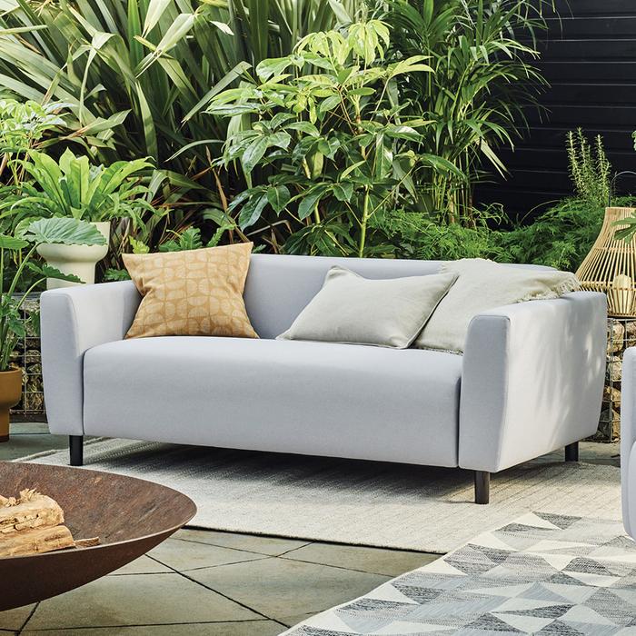 Light grey garden sofa with scatter cushions surrounded by green plants
