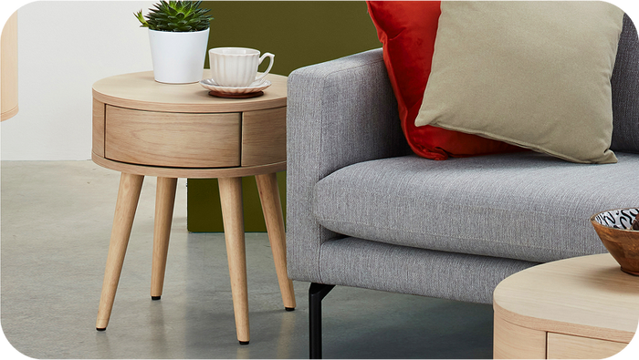 Light wood round side table next to a fabric grey sofa