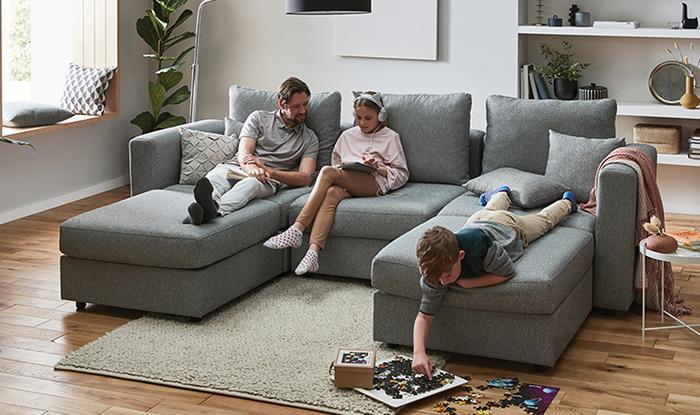 Young family sat on a u shaped sofa reading a book and magazine