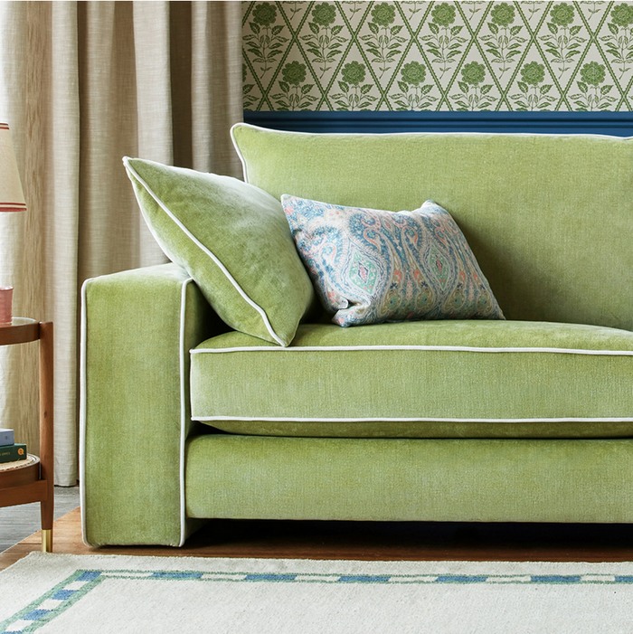 close up of a green fabric sofa with white piping along the edge
