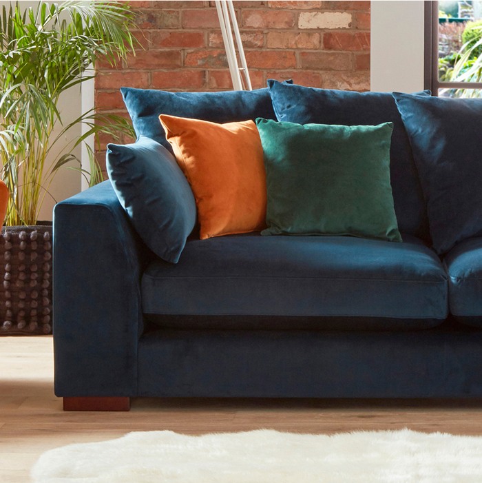close up shot of a blue velvet sofa with orange, green and blue scatter cushions