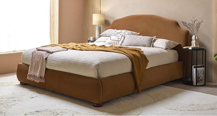 Battersea bed upholstered in tan velvet, dressed with cream bedding and a mustard throw