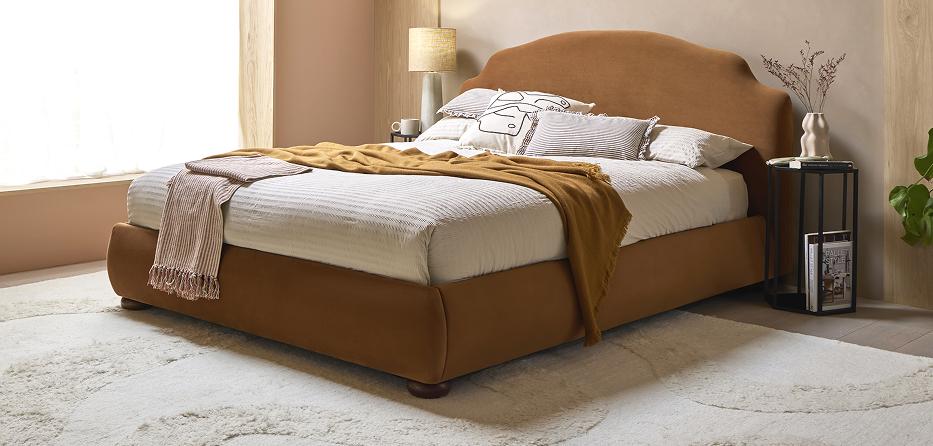 Battersea bed upholstered in tan velvet, dressed with cream bedding and a mustard throw