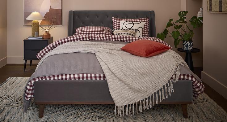 Chiswick bed upholstered in grey velvet, dressed with red gingham bedding and a cream throw